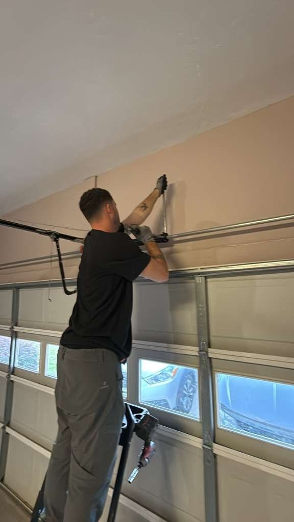 Technician in a dark polo reaching up to the overhead track of a garage door with window panels