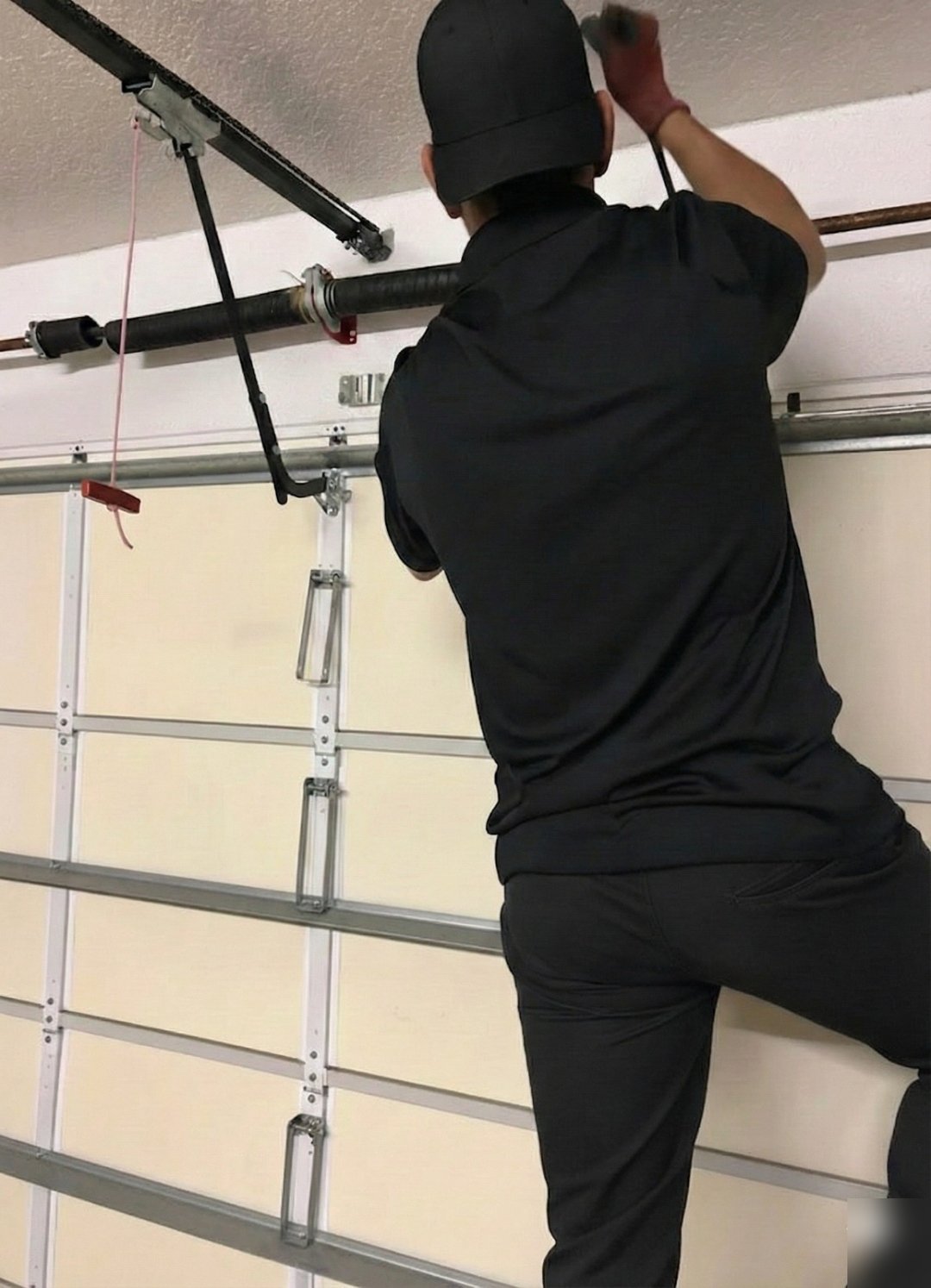 Technician on a ladder working at the top section of a sectional garage door