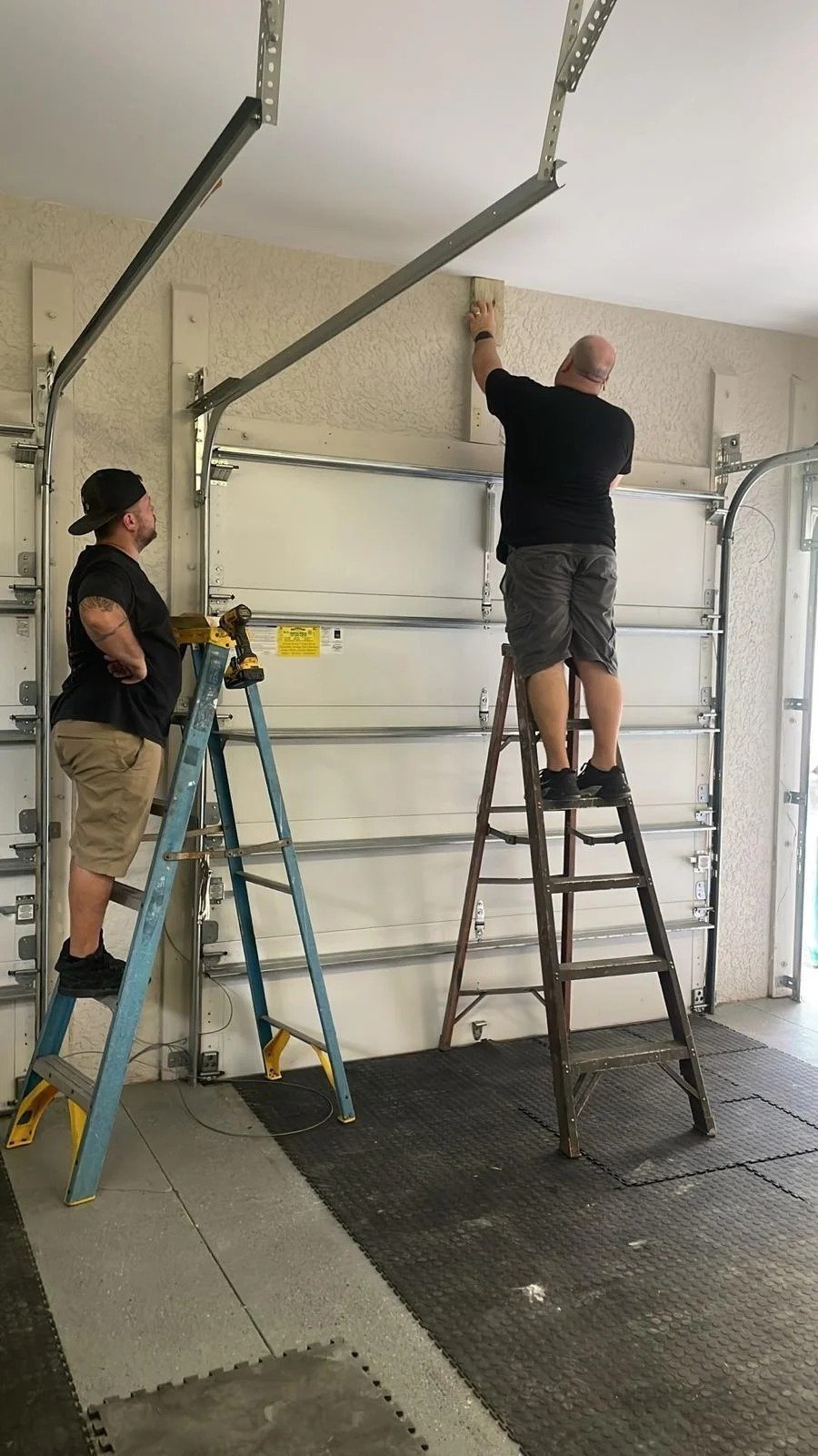 Two technicians on ladders adjusting the tracks of a garage door