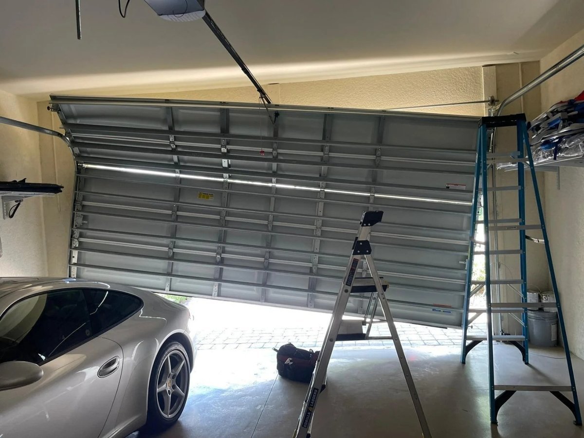 Garage door partway up above a silver car, with ladders and tools in the garage