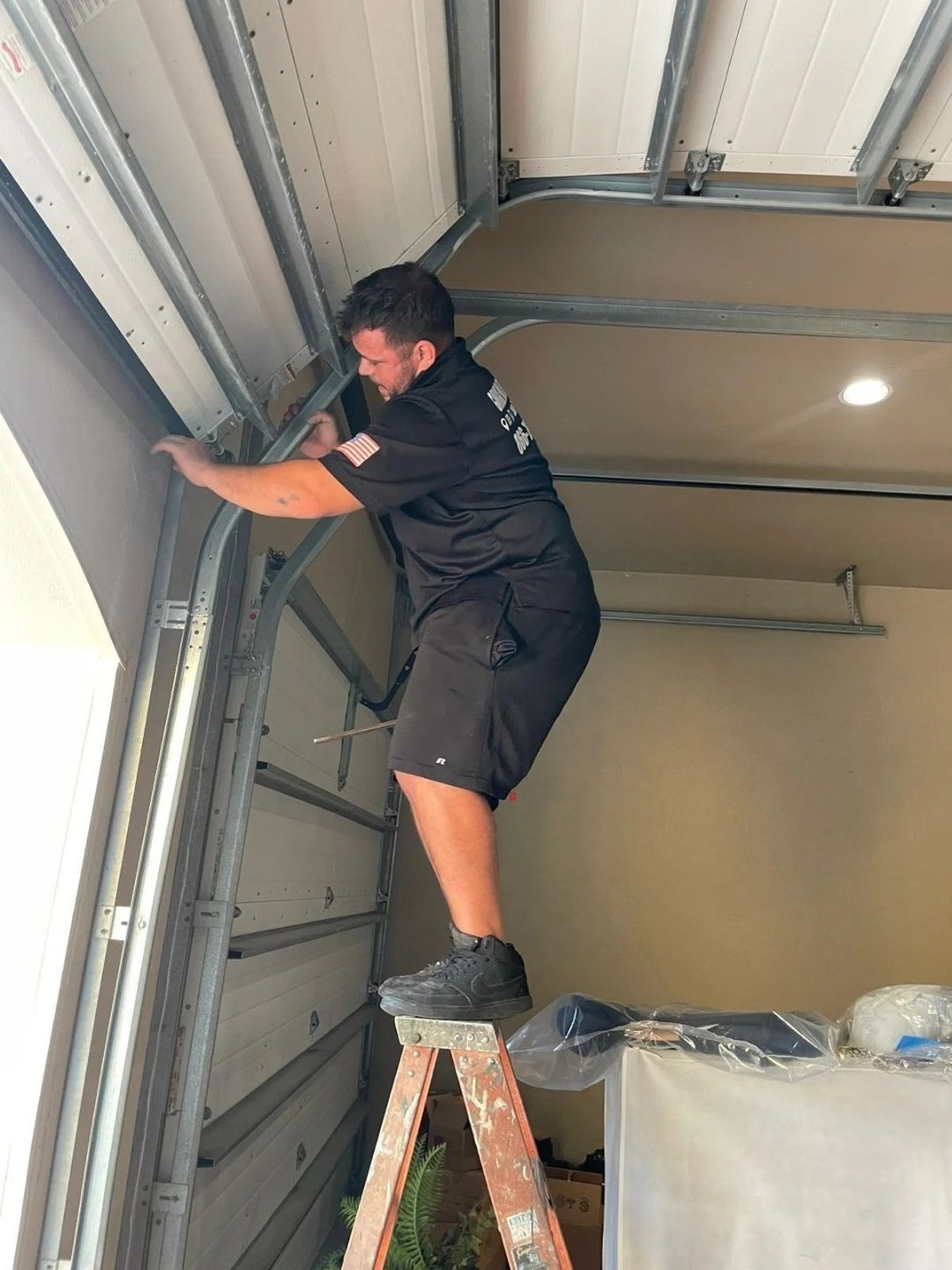 Technician on a stepladder reaching up to the side track of a garage door