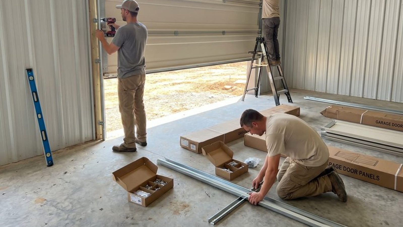 Two installers laying out garage door track and hardware boxes on a garage floor