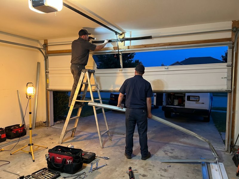 Technician on a ladder and a second worker below a half-open garage door in evening light