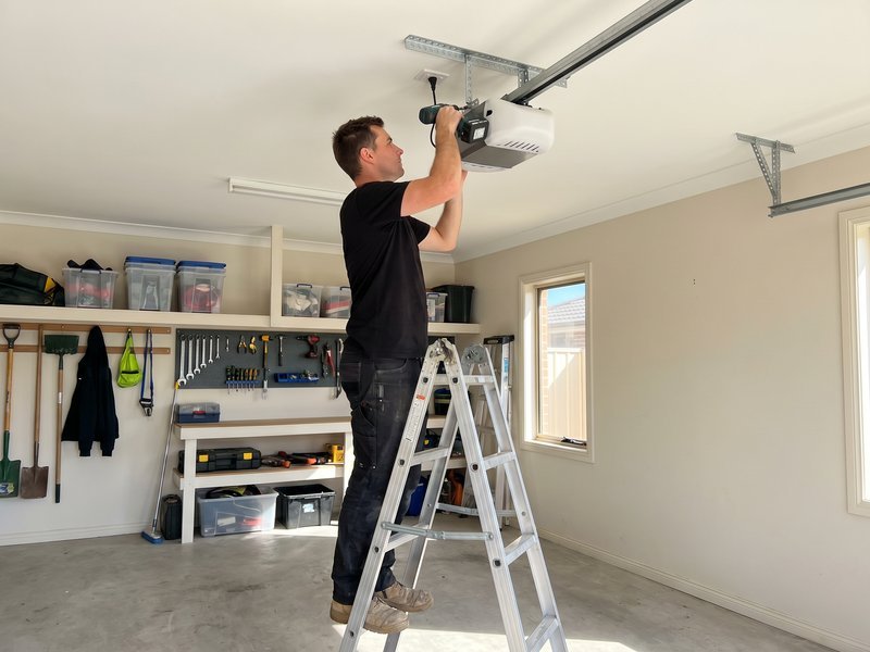 Technician on a stepladder mounting a garage door opener at the ceiling