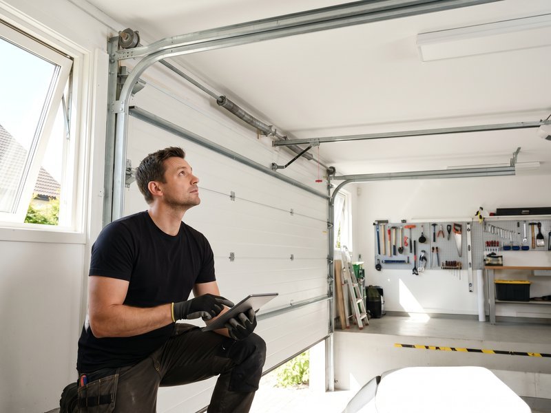 Technician kneeling beside tools while checking a tablet in a garage