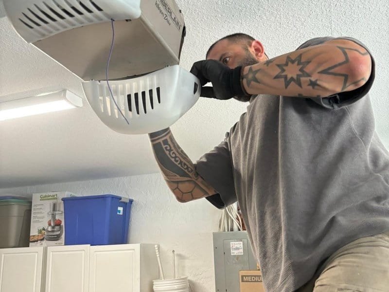 Technician with a tattooed forearm working on the opener head at the garage ceiling