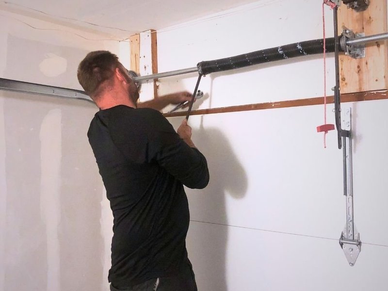 Technician working on a bracket at the top of a garage door where the spring bar is mounted